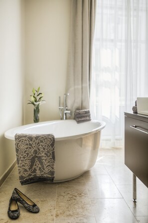 A modern bathroom with a freestanding bathtub, a vanity with a mirror, and a vase with flowers on the wall. - Residence Wollzeile (Vienna)