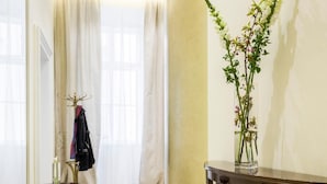 A hallway with a marble floor, a coat rack with a jacket, a small table with a candle, and a vase with flowers. - Residence Wollzeile (Vienna)