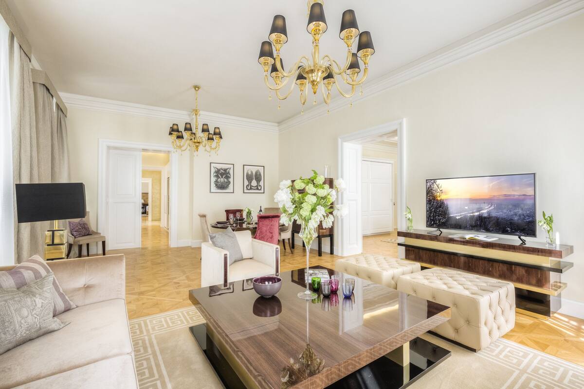 A spacious living room with a large flat-screen TV, a wooden coffee table, and a chandelier.