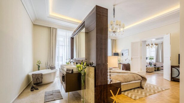 A modern hotel room with a large bed, a sitting area, a bathroom with a bathtub, and a large mirror. - Residence Wollzeile (Vienna)