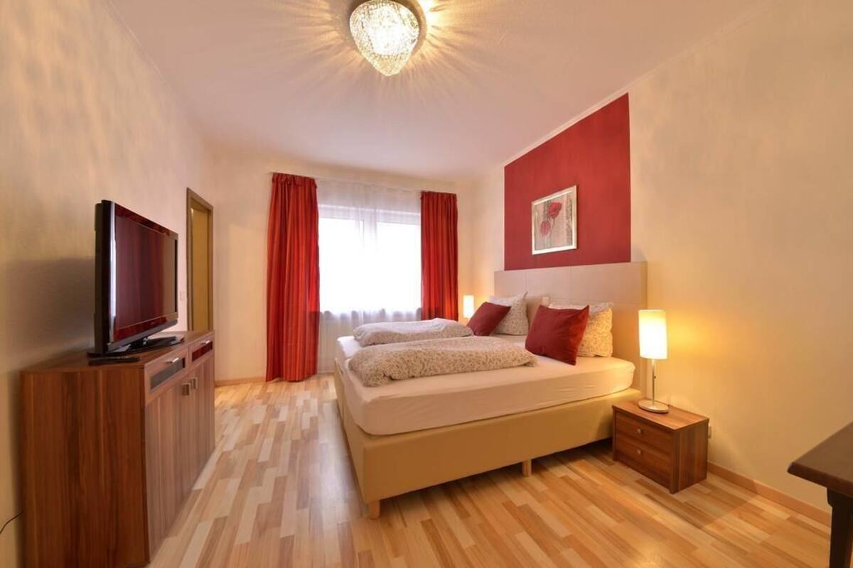 A hotel room with a bed, a TV, a nightstand, and a lamp.