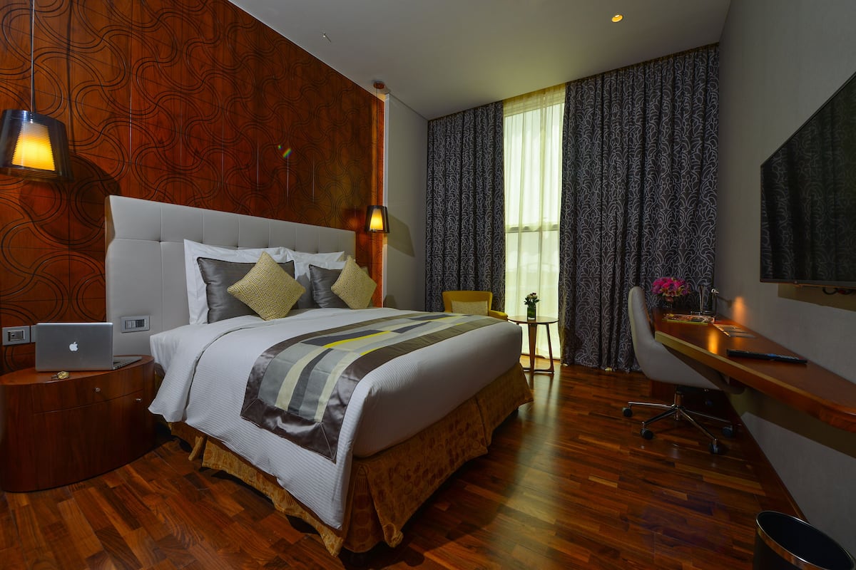 Een hotelkamer met een groot bed, een bureau, een stoel, een laptop op een nachtkastje en een raam met gordijnen.