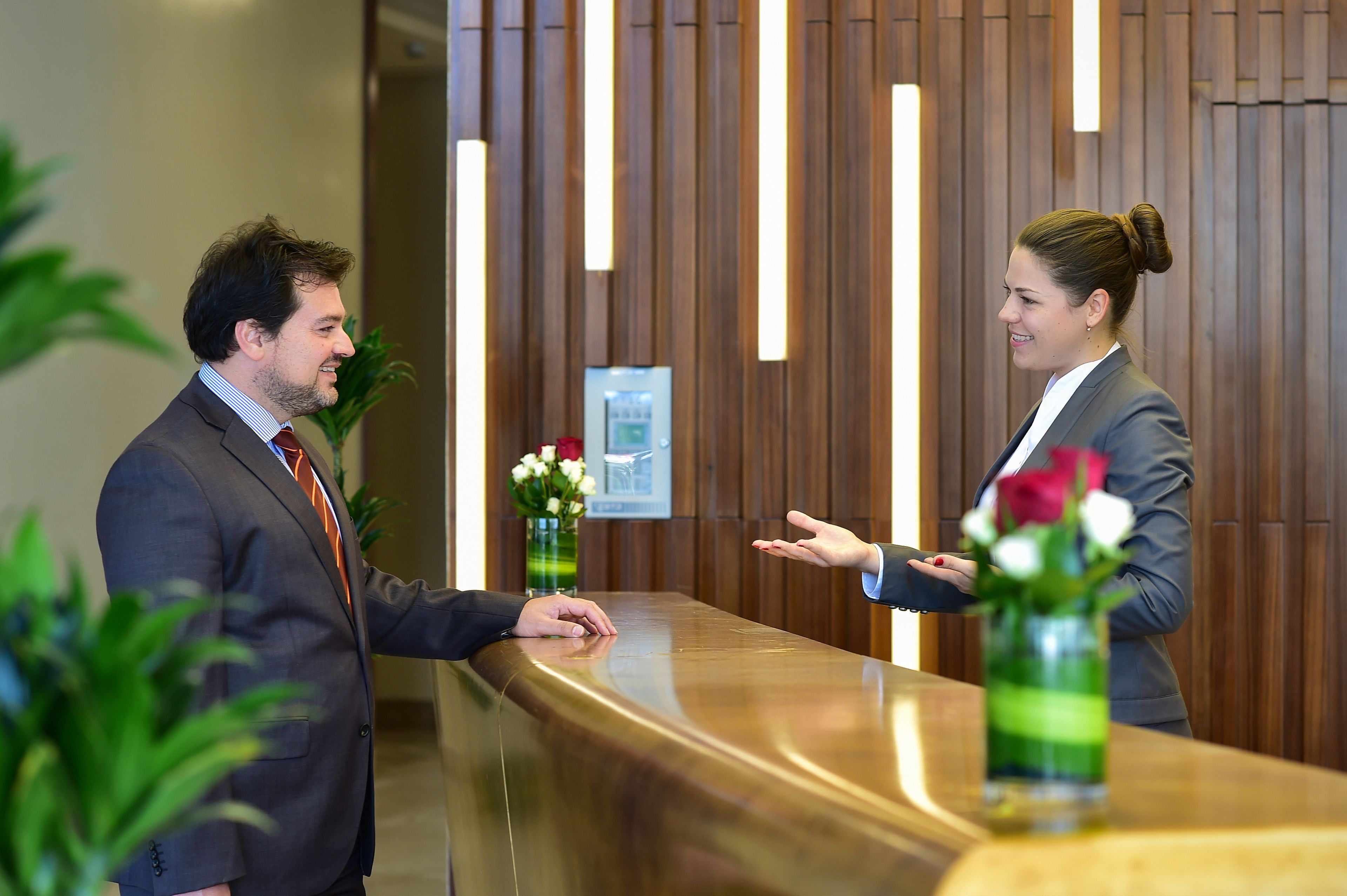 A reception area with a wooden reception desk, a framed picture on the wall, and two vases with flowers.
