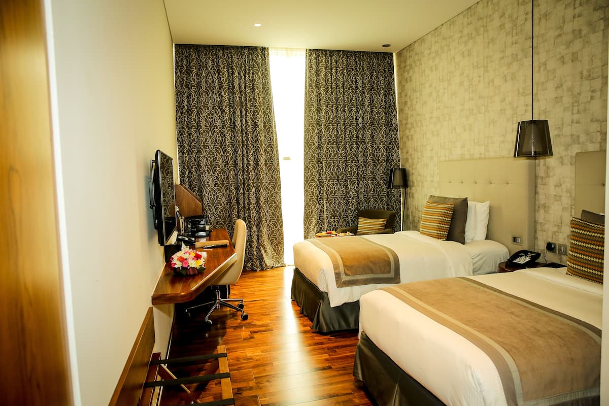 Een hotelkamer met twee bedden, een bureau met stoel, een televisie en een telefoon.