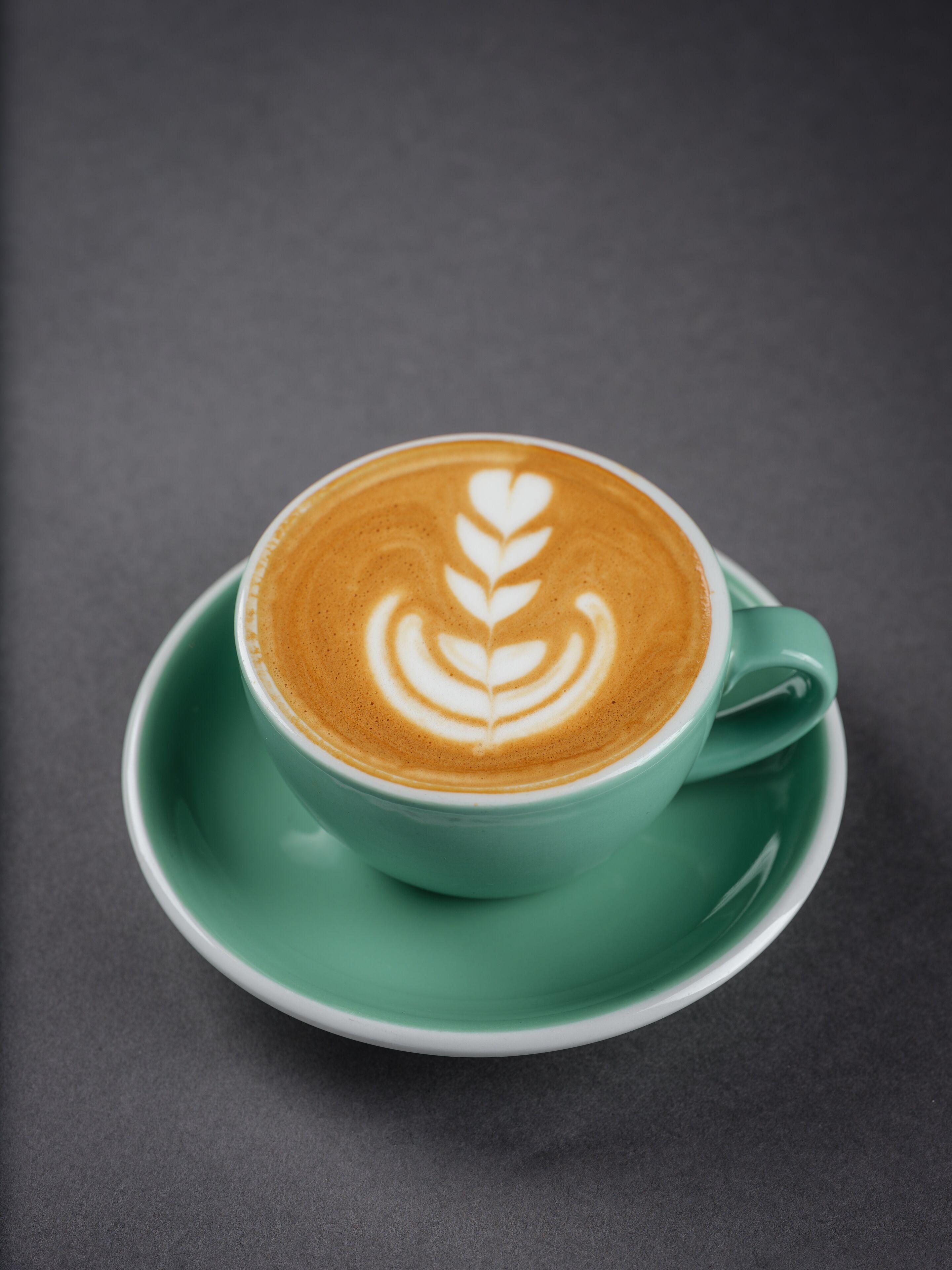 A cup of coffee with latte art on a green saucer.