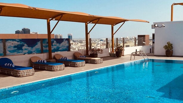 A rooftop pool with lounge chairs and a city view. - The Avenue Hotel (Doha)