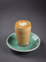 Una taza de café con diseño de espuma de latte sobre un plato verde.