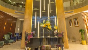 A lobby with a grand piano, a reception desk, and a large column. - The Avenue Hotel (Doha)