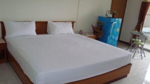 A hotel room with a large bed, a wooden headboard, a small table with a chair, and a blue cabinet. - Cosy Place Hatyai (Hat Yai)