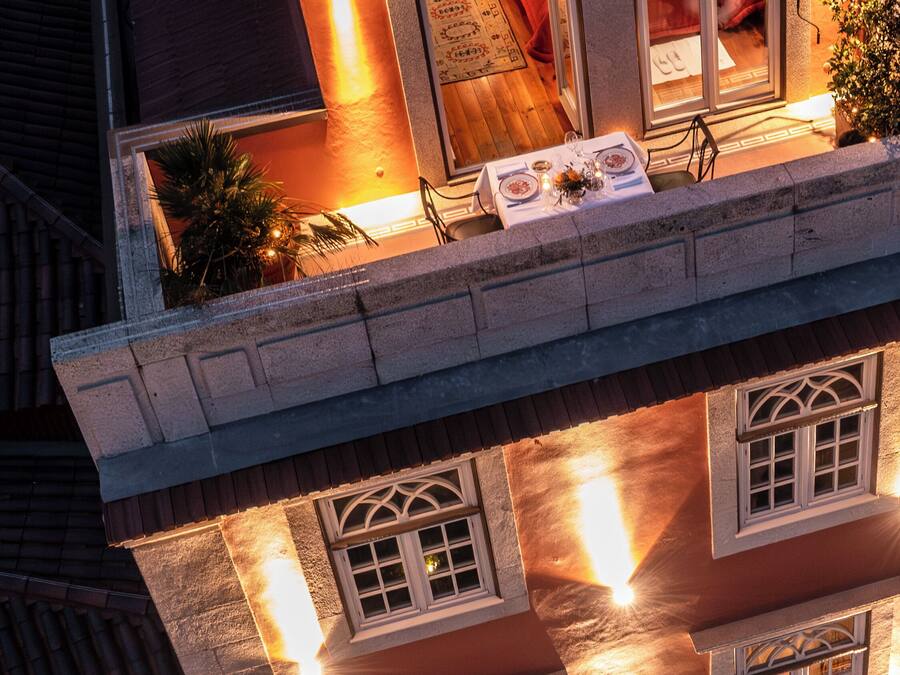 Un bâtiment traditionnel doté de nombreuses fenêtres, d’un balcon avec une table dressée pour le dîner, et d’un intérieur chaleureux et bien éclairé.