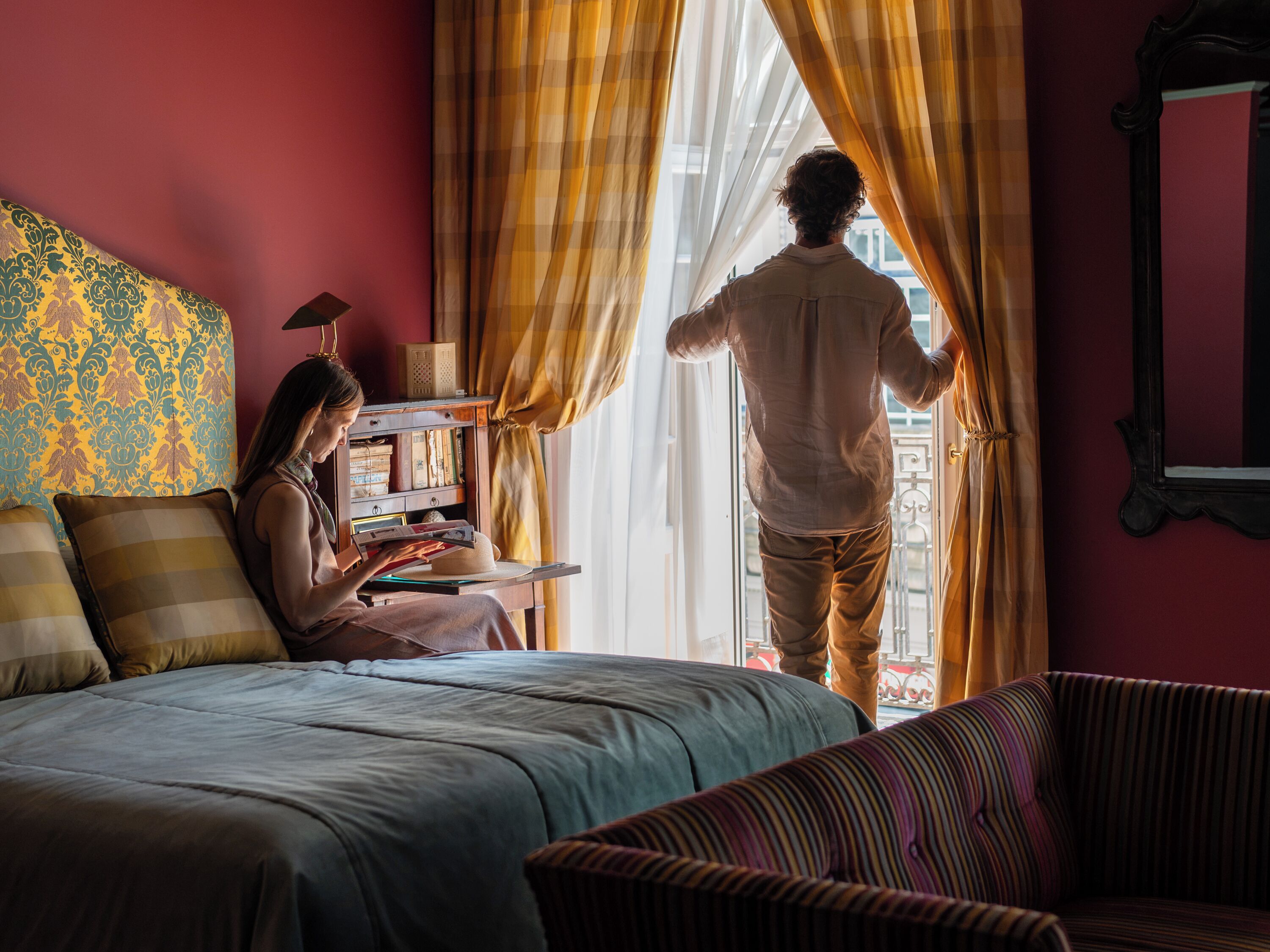 Un dormitorio con cama, una silla, una estantería y una ventana con cortinas.