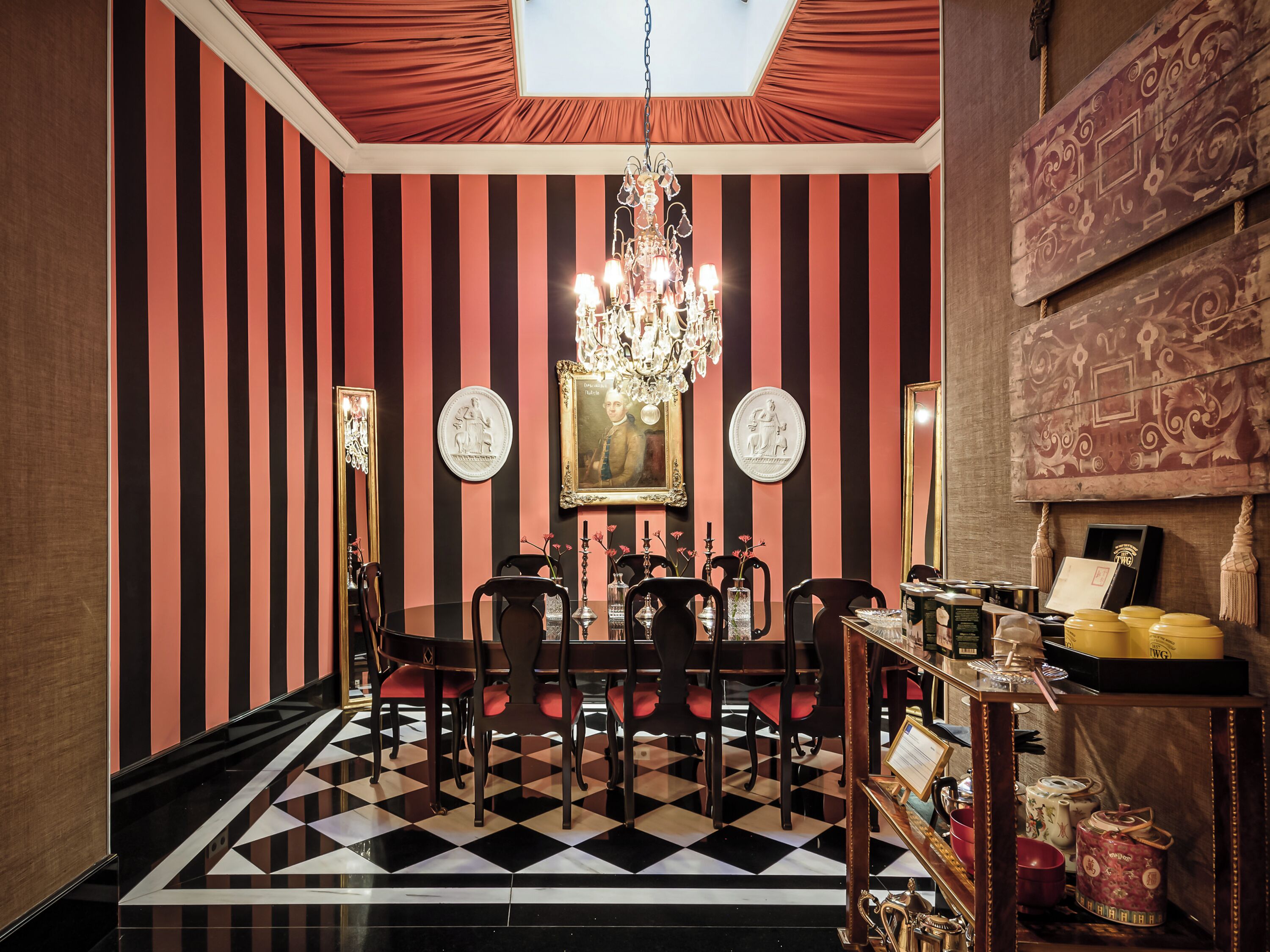 A dining area with a checkered floor, striped walls, a chandelier, and a table with chairs.