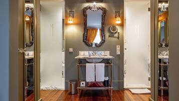 Une salle de bain avec un lavabo en marbre, deux miroirs fixés au mur, un porte-serviettes et une poubelle.