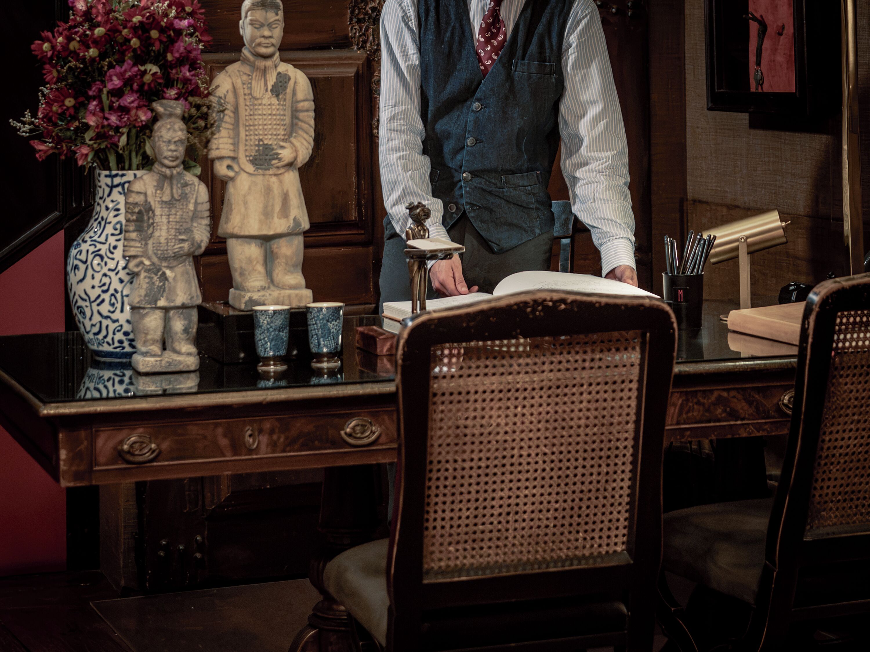 A wooden desk with a vase of flowers, a statue, and a book.