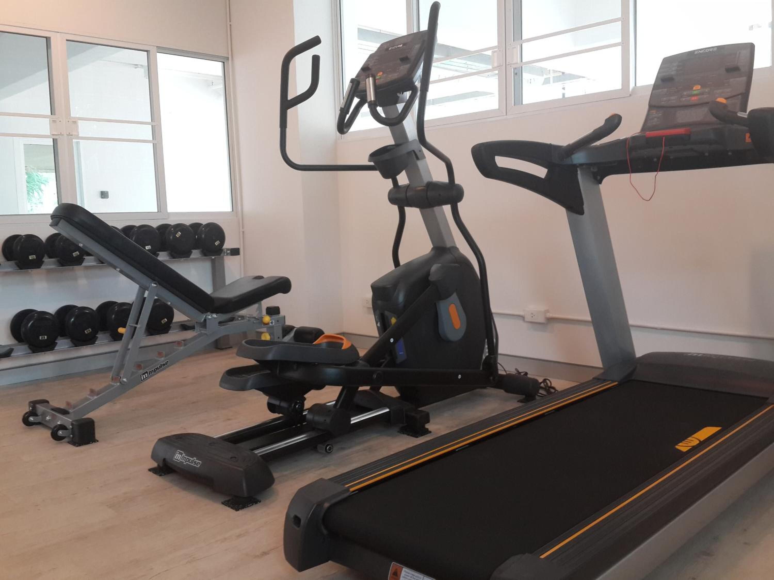 Un gimnasio con equipo cardiovascular, que incluye una cinta de correr, elíptica y prensa de banca.