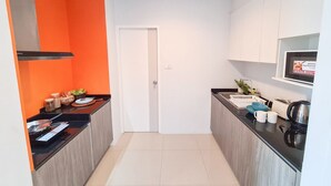 A narrow kitchen with a white door, black countertops, and a tiled floor. - Des Res Hotel and Residence (Samut Prakan)
