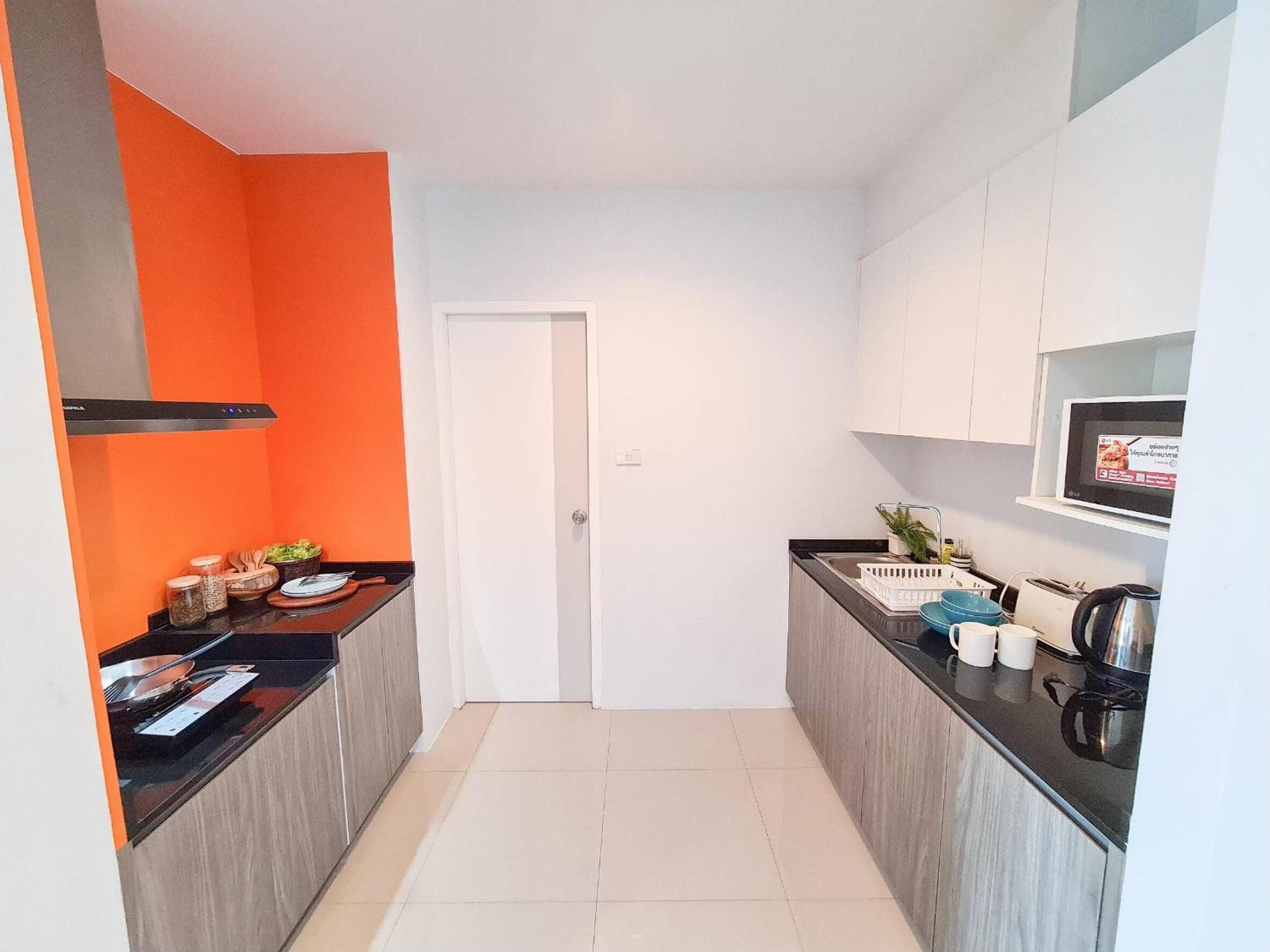 A narrow kitchen with a black countertop, white cabinets, and a door leading to another room.
