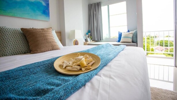 A hotel room with a large bed, a balcony with a view, and a painting on the wall. - Des Res Hotel and Residence (Samut Prakan)