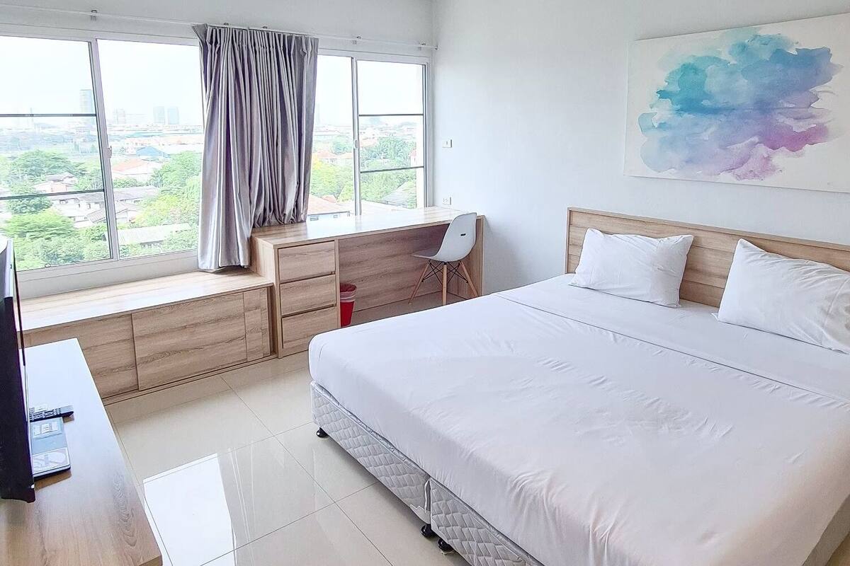 Ein modernes Hotelzimmer mit einem großen Bett, einem Schreibtisch mit Stuhl, einem Fenster mit Vorhängen und Blick auf die Stadt.