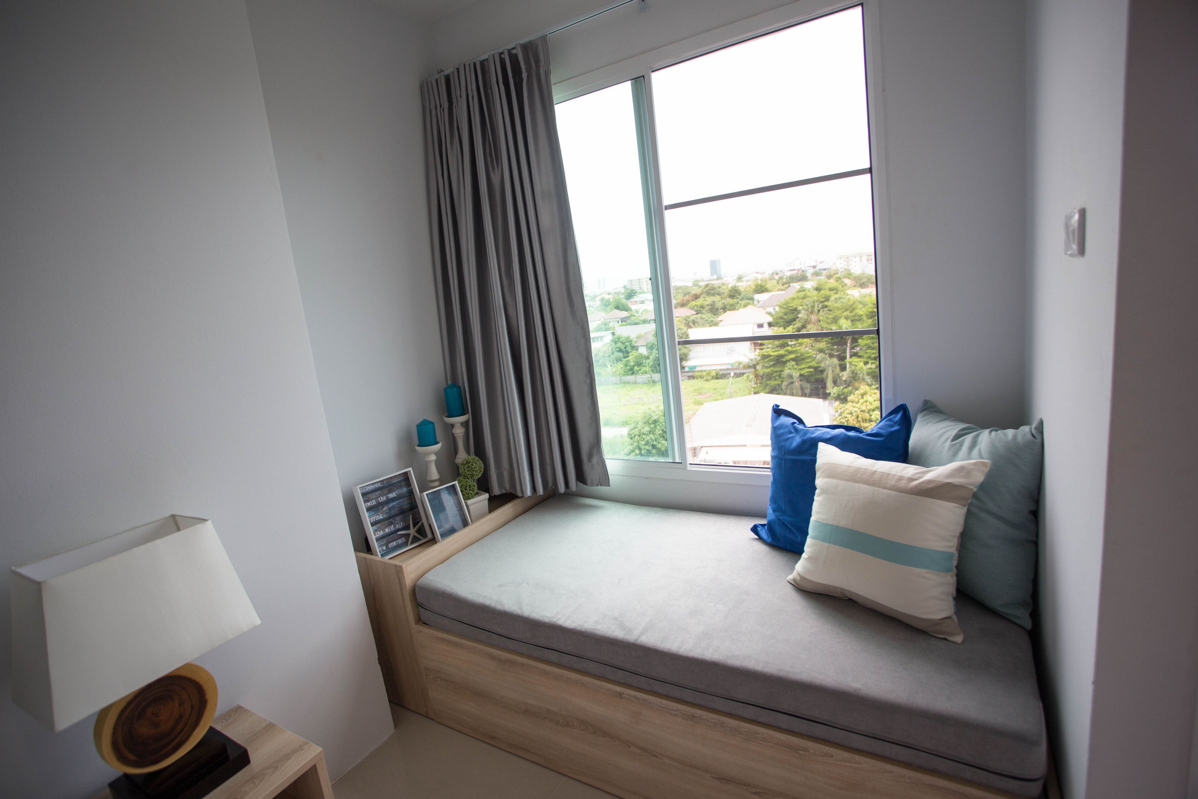 A cozy room with a built-in bench by a large window, a lamp on a side table, and a view of greenery outside.