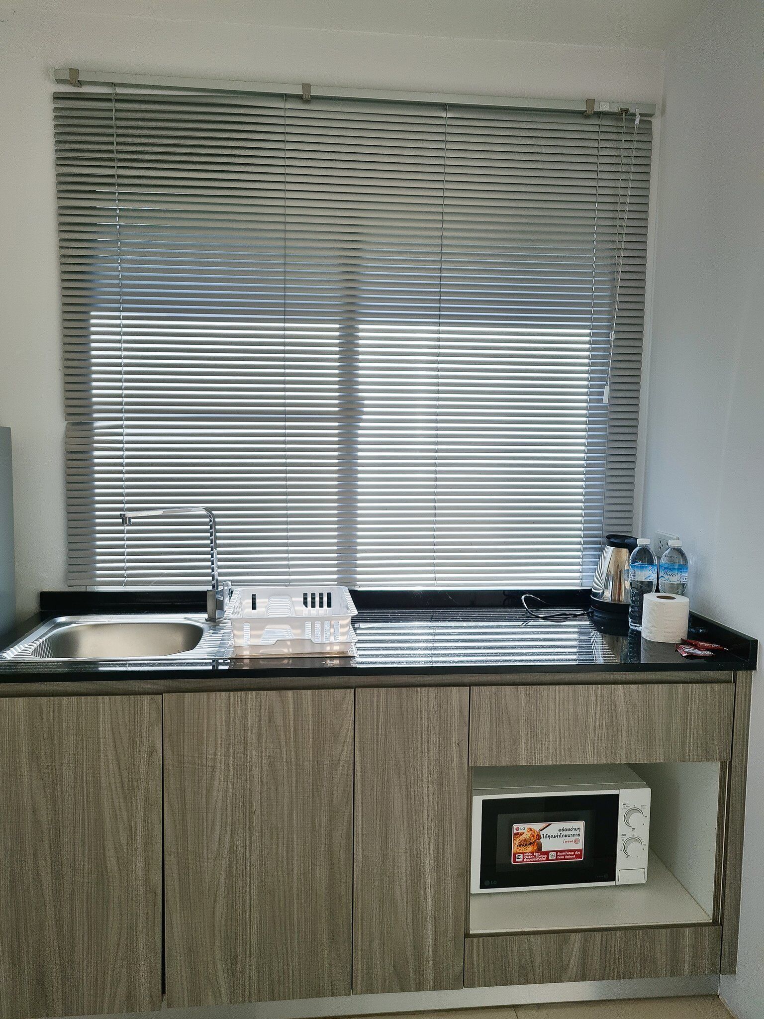 A kitchen with a built-in microwave, a sink, and a window with blinds.