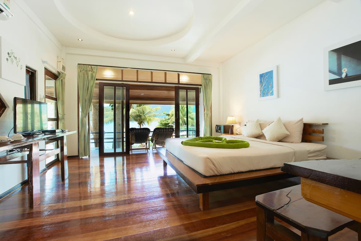 Habitación de hotel con cama, escritorio, silla, televisión y vistas a palmeras.