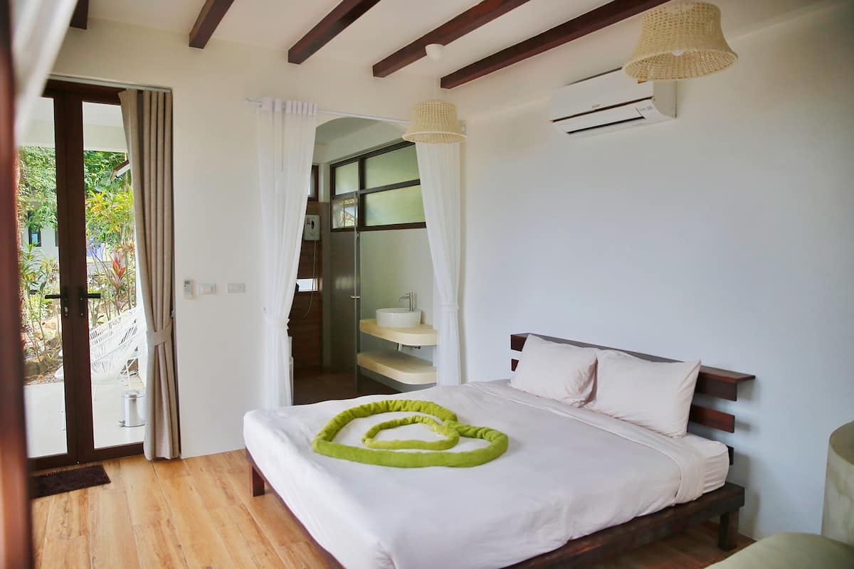 Un dormitorio con cama, un banco de madera, un baño con lavamanos y vistas al exterior.