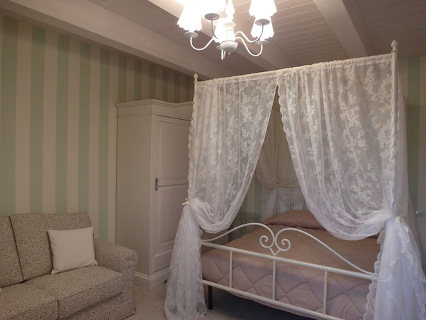 A bedroom with a four-poster bed, a nightstand, a wardrobe, and a patterned sofa.