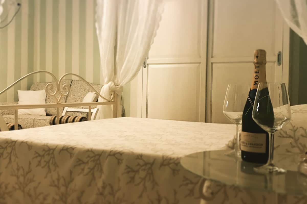 A room with a bed, a table with a bottle of champagne and a glass, and a wardrobe.