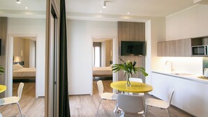 A modern kitchen with a flat-screen TV, a dining area with a yellow table, and a bed in the background. - Hotel Hollywood (Rimini)