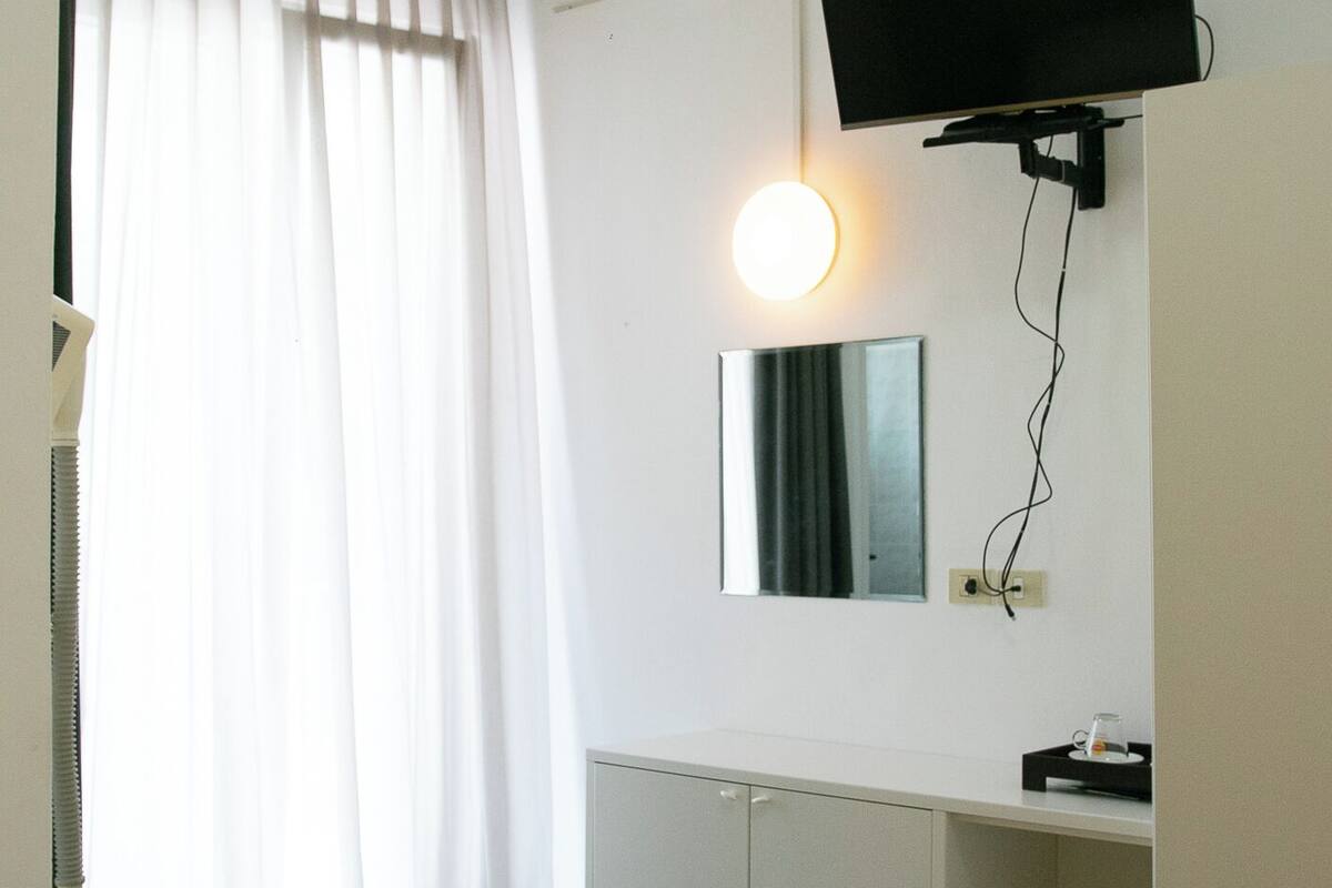 A hotel room with two beds, a TV mounted on the wall, a mirror, and a bedside table.