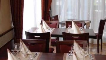 Un restaurante con mesas dispuestas, servilletas blancas, sillas rojas y vistas a través de cortinas traslúcidas.