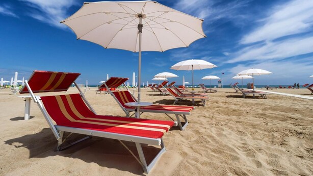 A beach with rows of red and white striped lounge chairs and white umbrellas. - Hotel Hollywood (Rimini)