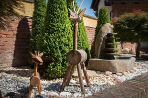 A garden with wooden animal sculptures, a brick wall, and a stone fountain. - Casa Del Grande Vecchio (Airasca)