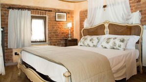 A bedroom with a large bed, a wooden headboard, a nightstand, a wall-mounted lamp, and a window with curtains. - Casa Del Grande Vecchio (Airasca)
