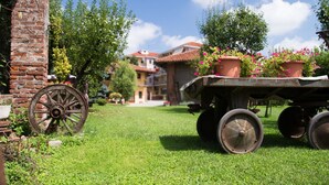 A rustic outdoor setting with a wooden cart, a brick wall, and a building with a tiled roof in the background. - Casa Del Grande Vecchio (Airasca)