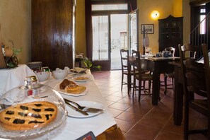 A dining area with a long table set for a meal, featuring a pie and plates, and a wooden cabinet in the background. - Casa Del Grande Vecchio (Airasca)