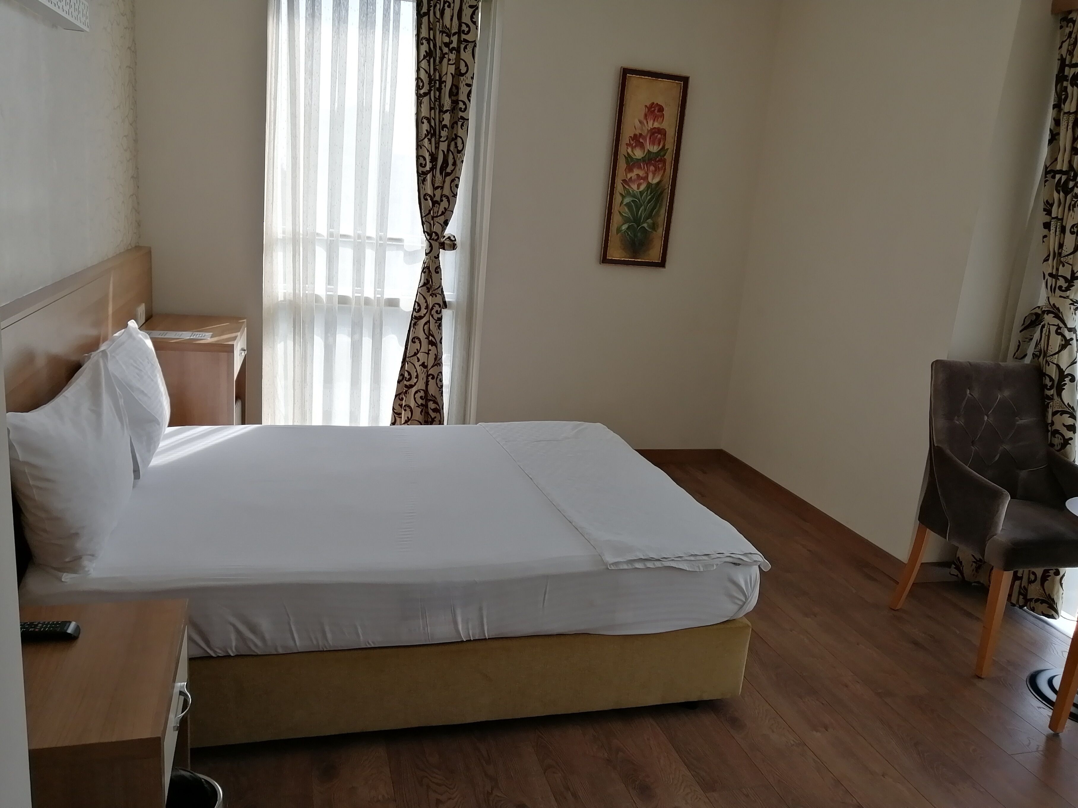 A hotel room with a bed, a chair, a bedside table, and a painting on the wall.
