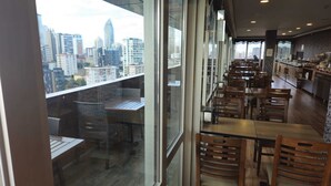 Un restaurante con vista a la ciudad, mesas y sillas de madera, y una cocina visible a través del ventanal.