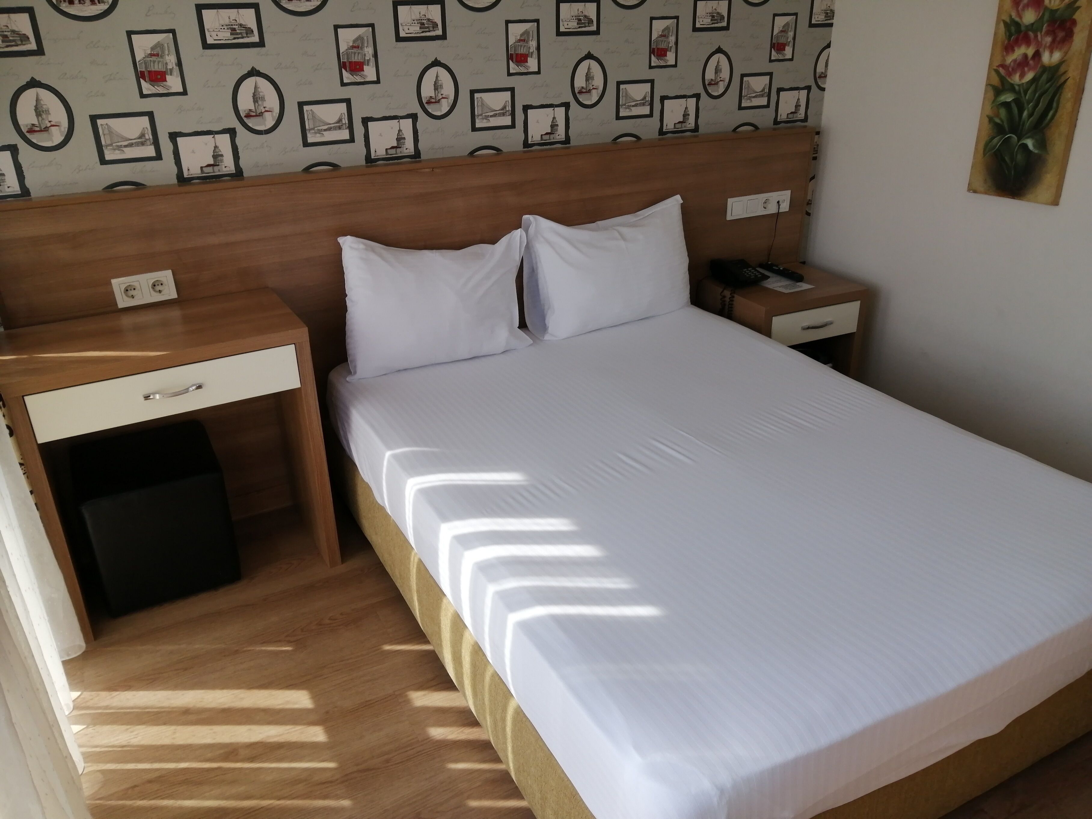 A neatly made bed with white linens, a wooden headboard, and a nightstand with a phone and a lamp.