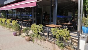 Un espacio al aire libre con mesas, sillas, un toldo cubierto y plantas en macetas.