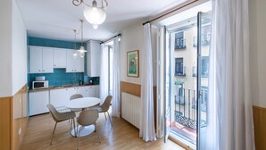 A modern kitchen with white cabinets, a dining table with chairs, and a view of a balcony with white curtains. - Oriente Suites (Madrid)