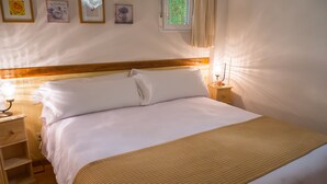 A neatly made bed with white linens and a beige blanket, a bedside table with a lamp, and a wall with framed pictures. - Oriente Suites (Madrid)