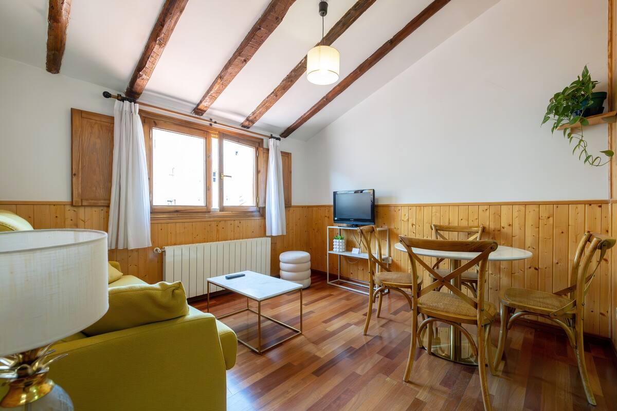 Une pièce chaleureuse avec un plancher en bois, une télévision, une table à manger avec des chaises, un canapé et une lampe.