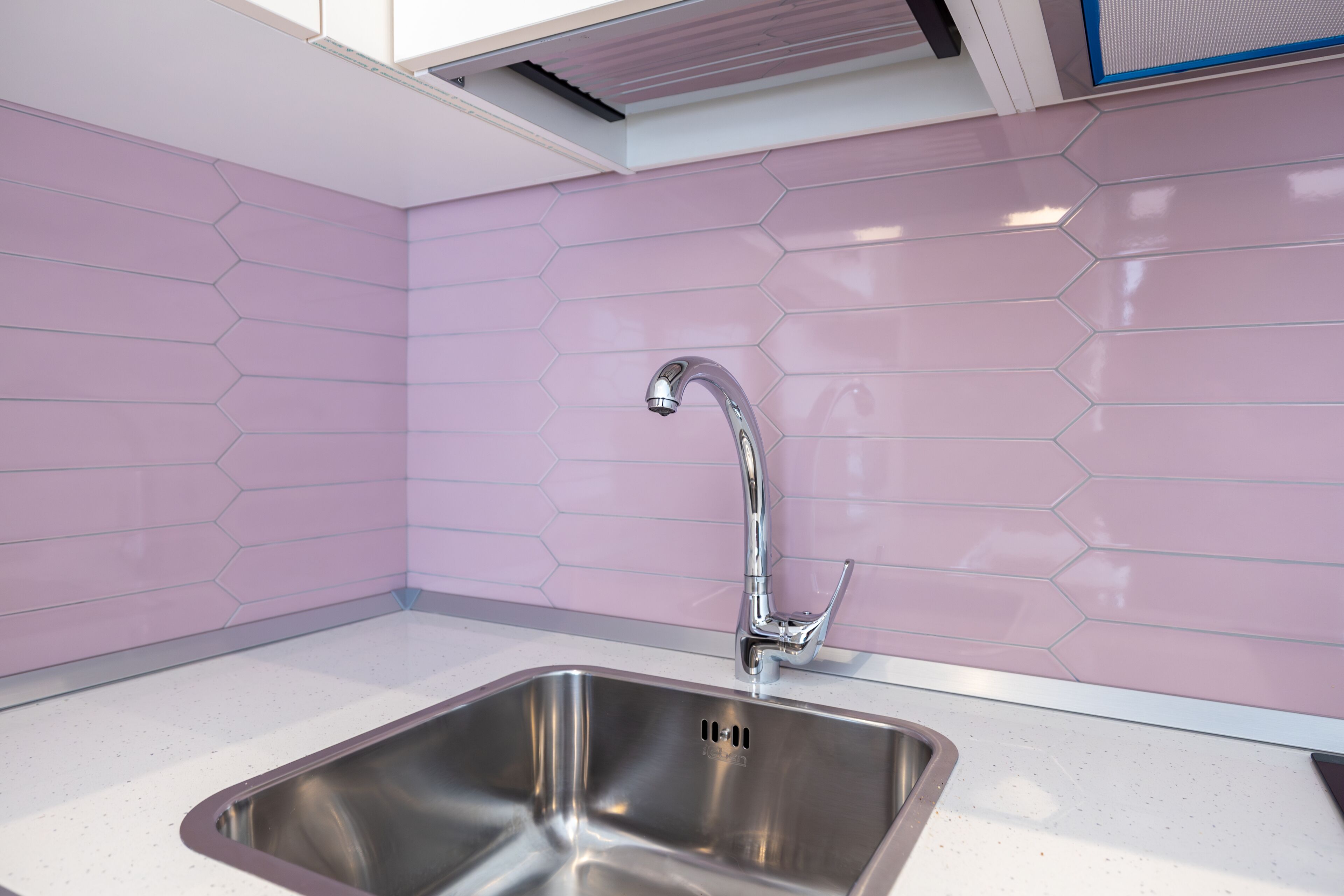 Una cocina moderna con un lavamanos de acero inoxidable, encimera blanca y baldosas hexagonales rosas.