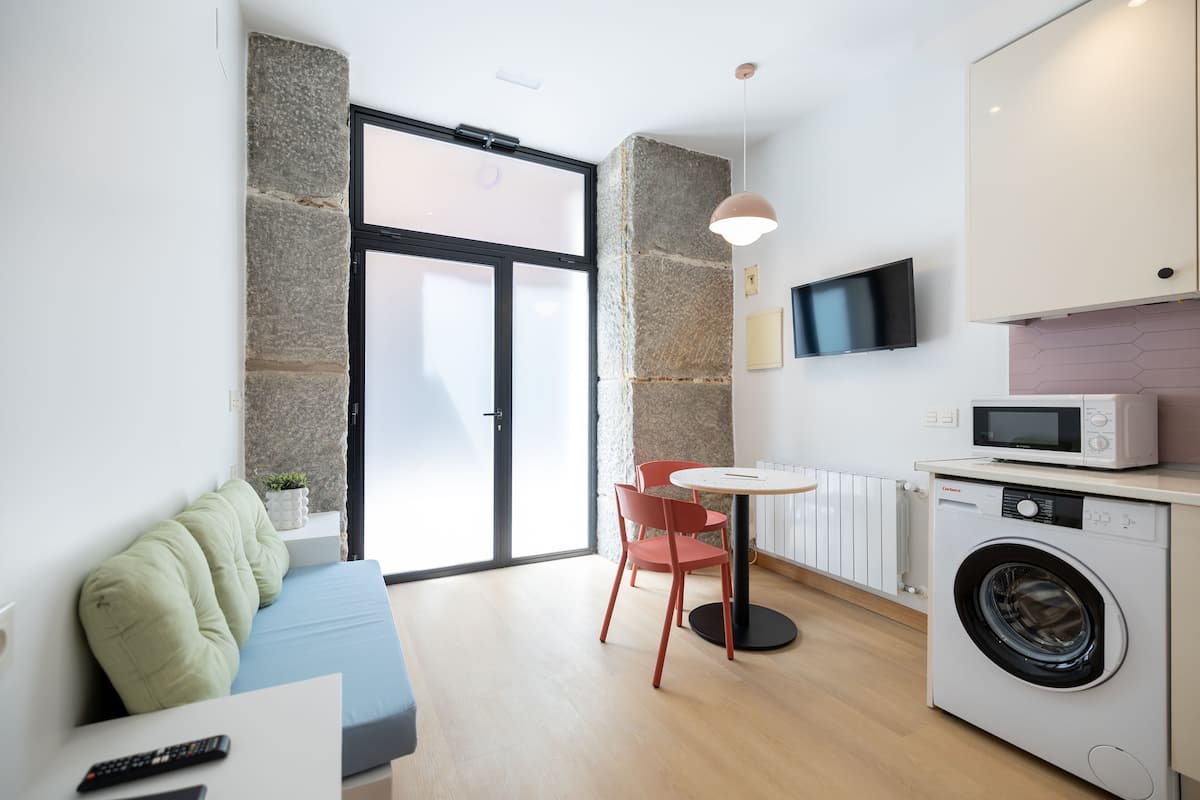 Un espace de vie compact comprenant un canapé, une table à manger, des chaises, un lave-linge et un téléviseur fixé au mur.