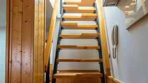 A wooden staircase with a handrail and a wall-mounted phone. - Oriente Suites (Madrid)