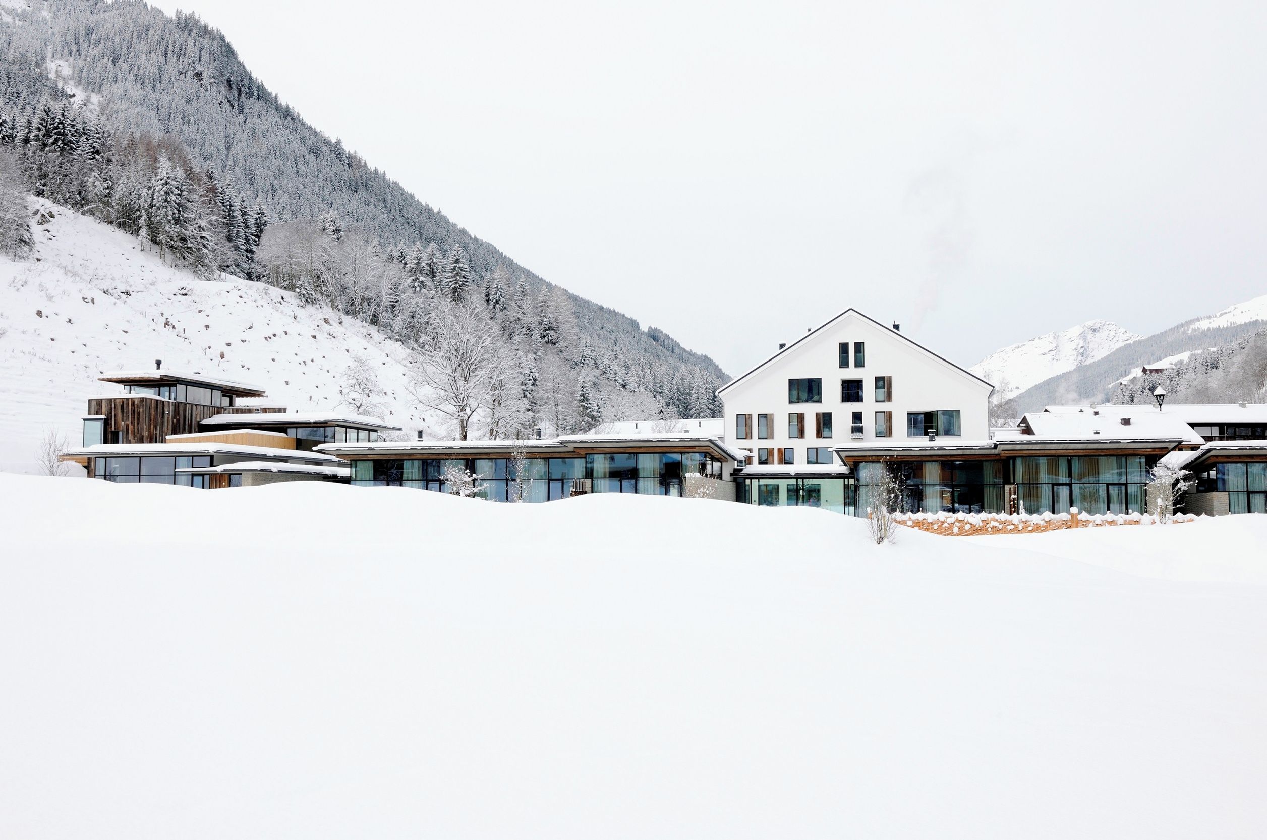 A modern hotel with a large central building and smaller structures, surrounded by snow-covered mountains.