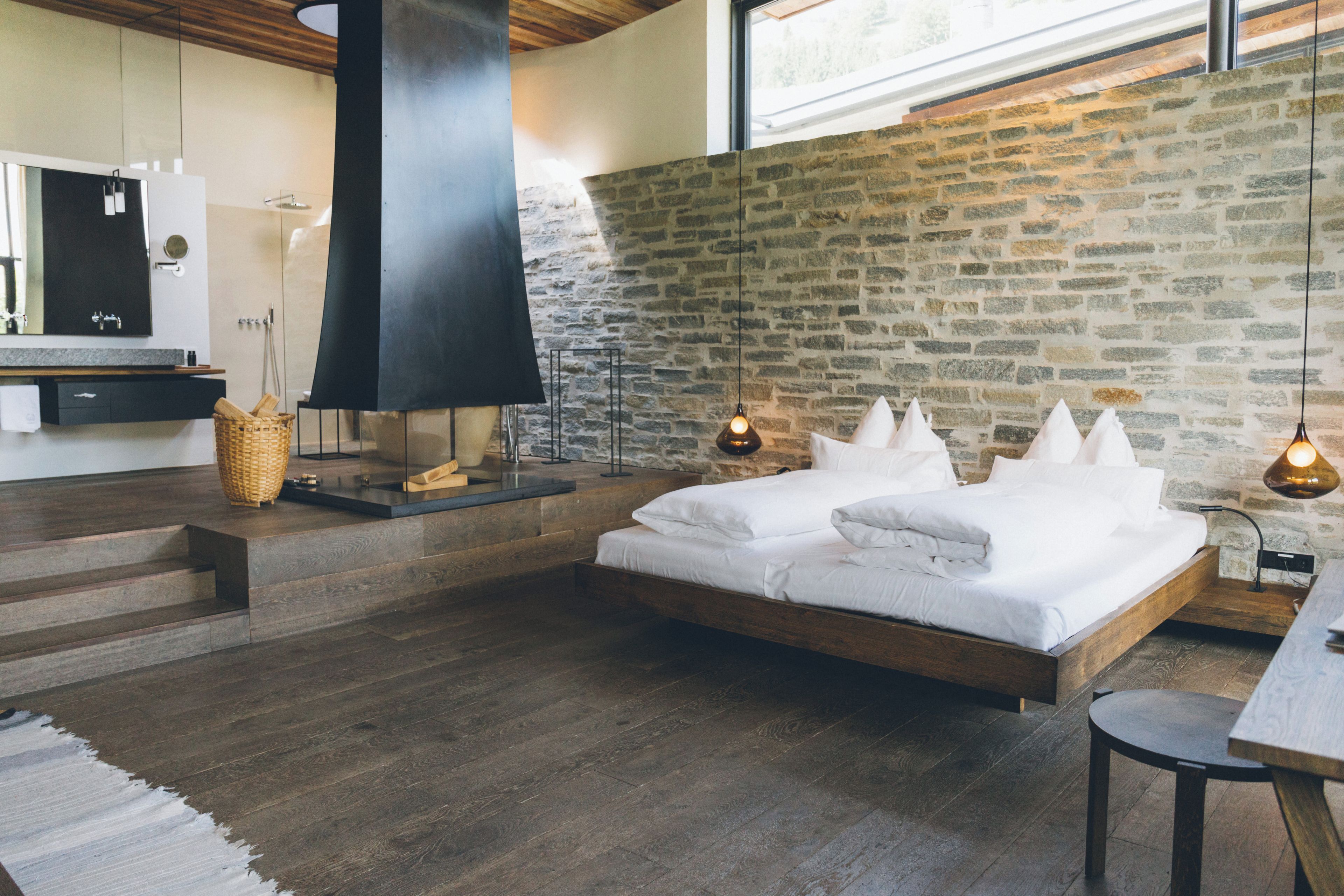 A modern bedroom with a large bed, a stone wall, and a wooden floor.