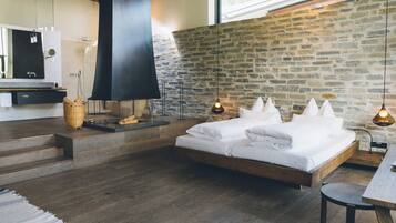 A modern bedroom with a large bed, a stone wall, and a wooden floor.